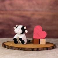 A sitting black and white cow that is 5 inches tall while sitting next to wooden blocks