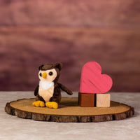 A stuffed owl that is 5 inches tall while sitting on top of a piece of wood