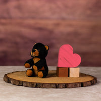 A black and brown bear that is 5 inches tall while sitting next to wooden blocks