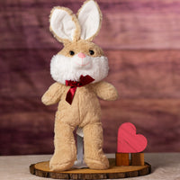 A beige rabbit that is 16 inches while standing wearing a red bow next to wooden blocks