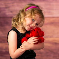 girl holding  red bright and cheery bear with bow around her neck
