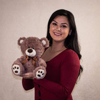 A woman holding a brown bear that is 10 inches tall while sitting with paw prints on its feet