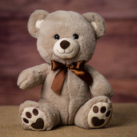 A beige bear that is 11 inches tall while sitting with paw prints on its feet