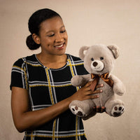 A woman holds a beige bear that is 11 inches tall while sitting with paw prints on its feet