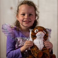A little girl holding a stripped tiger that is 10 inches tall while sitting