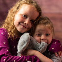 Two little girls holding a gray elephant that is 10 inches tall while sitting