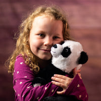 A little girl holding a black and white panda that is 10 inches tall while sitting