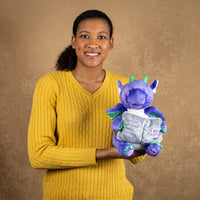 A woman holds a purple animated dragon that is 10.5 inches tall while sitting holding a storytelling book