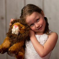 A little girl holding a brown lion that is 10 inches tall while standing