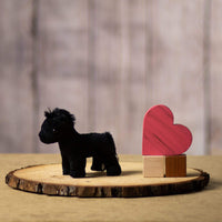 A small black horse stuffed animal sitting on a log slice with props