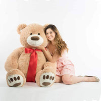 A woman next to a beige bear that is 60 inches tall while standing