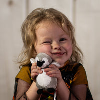 A little girl holding a gray penguin that is 5 inches tall while standing