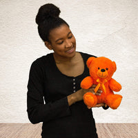 A woman holds a bright orange bear that's 9 inches tall while sitting