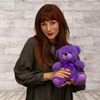 A woman holds a purple bear that is 9 inches tall while sitting