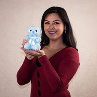 An adult woman smiles while holding a light blue bear in her hand