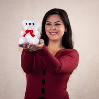 A woman holding a white bear that is 6 inches tall while sitting