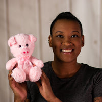A woman holding a light pink pig that is 7 inches tall while sitting wearing a matching bow