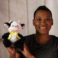 A woman holding a black and white cow that is 7 inches tall while sitting wearing a yellow bow