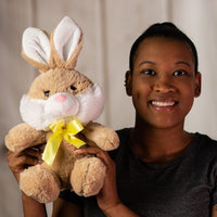 A woman holding a beige rabbit that is 10 inches while sitting wearing a yellow bow