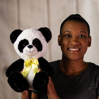 A woman holding a black and white panda that is 10 inches tall while sitting wearing a yellow bow