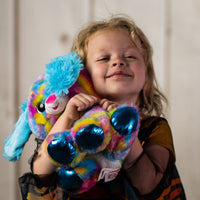 A little girl holding a psychedelic dog that is 10 inches tall while sitting with shiny paws , blue feathered ears, and sparkly eyes