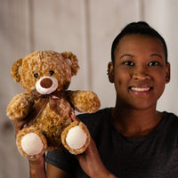 A woman holding a two-toned brown bear that is 10 inches tall while sitting wearing a brown bow
