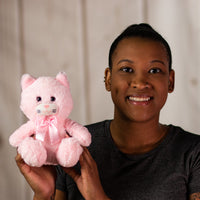A woman holding a light pink cat that is 7 inches tall while sitting wearing a matching bow