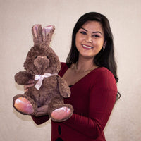 A woman holds a brown bunny with pinkish trim that is 12 inches tall while sitting