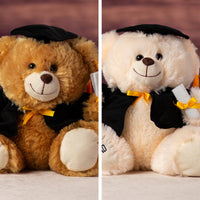 A brown and cream bear sporting a cape, diploma, hat and even the words #1 Grad embroidered on a paw 