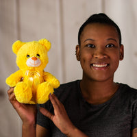 A woman holding a bright yellow bear that's 7 inches tall while sitting wearing a matching bow