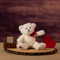 A cream bear that is 7 inches tall while sitting with a heart at the bottom of its foot next to wooden blocks