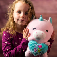 A girl holding a pink unicorn that is 10.5 inches tall while sitting holding valentine heart