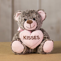 A brown bear that is 9 inches tall while sitting holding a pink heart that says "Kisses"