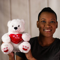 A woman holding a white polar bear that is 10 inches tall while sitting holding a red "BE MINE" heart with embroidered red hearts on its feet