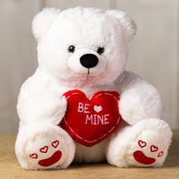 A white polar bear that is 14 inches tall while sitting holding a red "BE MINE" heart with embroidered red hearts on its feet