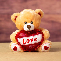 A beige bear that is 10 inches tall while sitting with glittery feet and ears holding a glittery red "LOVE" heart